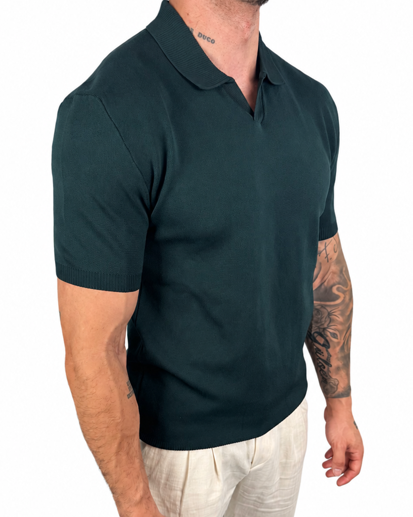 A man wearing a dark green short-sleeve polo shirt and off-white trousers, shown from the neck down against a plain white background.