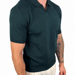 A man wearing a dark green short-sleeve polo shirt and off-white trousers, shown from the neck down against a plain white background.