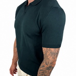 A man wearing a dark green short-sleeve polo shirt and off-white trousers, shown from a side profile against a plain white background.