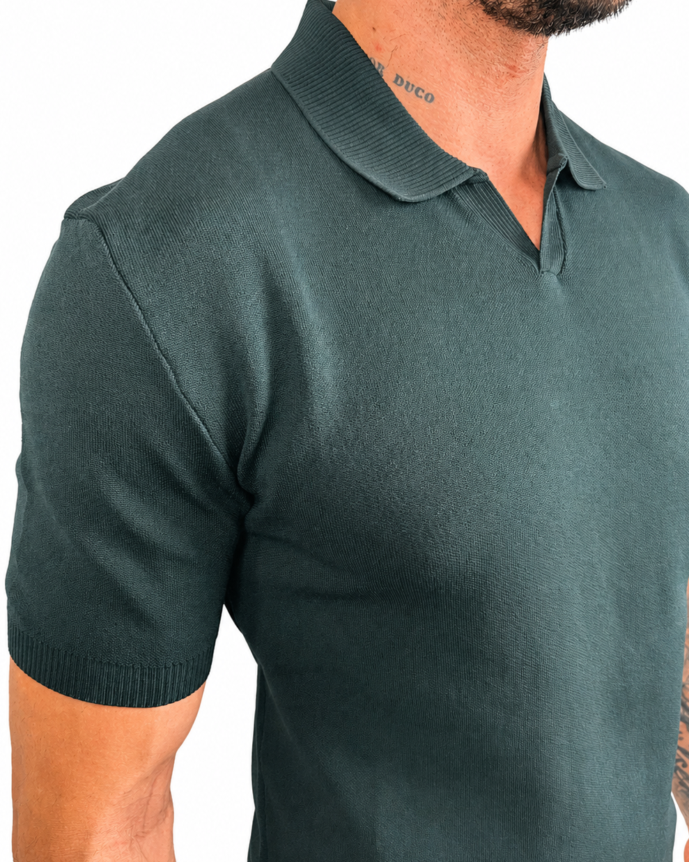 A close-up of a man wearing a dark green short-sleeve knit polo shirt against a plain white background.