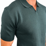 A close-up of a man wearing a dark green short-sleeve knit polo shirt against a plain white background.