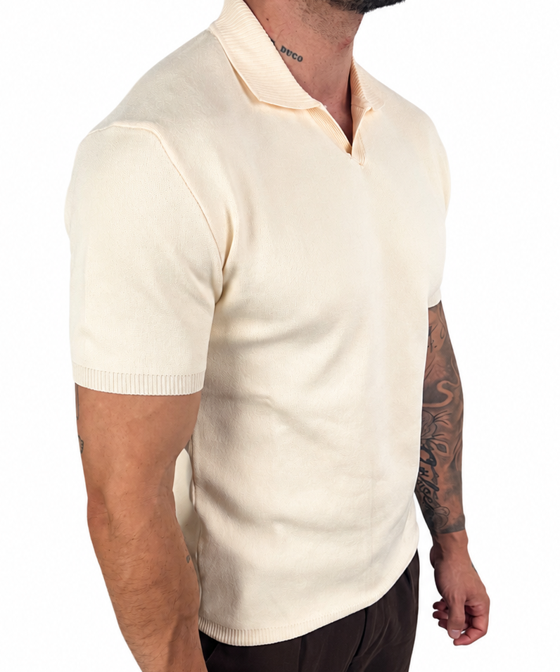A man wearing a cream-colored short-sleeve knit polo shirt and dark brown trousers, shown from a side profile against a plain white background.