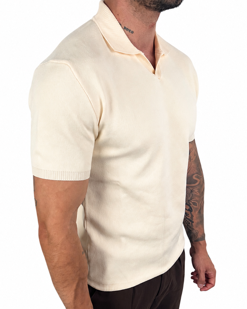 A man wearing a cream-colored short-sleeve knit polo shirt and dark brown trousers, shown from a side profile against a plain white background.