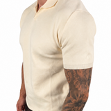 A man wearing a cream-colored short-sleeve knit polo shirt, dark brown pants, and white socks, shown from a side profile against a plain white background.