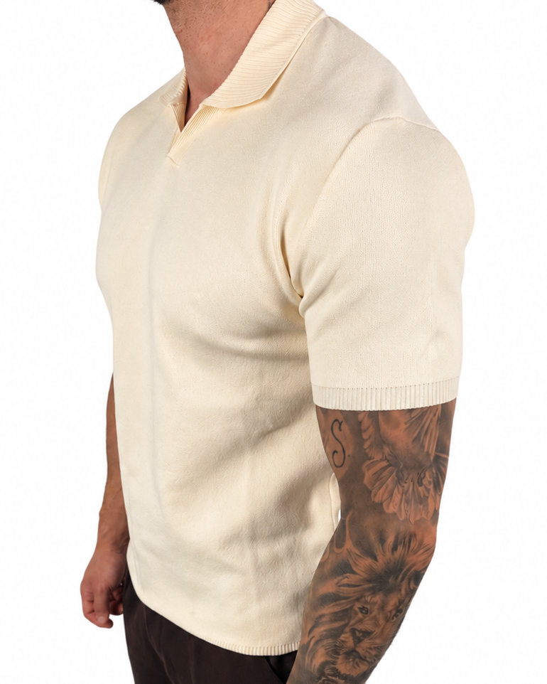 A man wearing a cream-colored short-sleeve knit polo shirt, dark brown pants, and white socks, shown from a side profile against a plain white background.