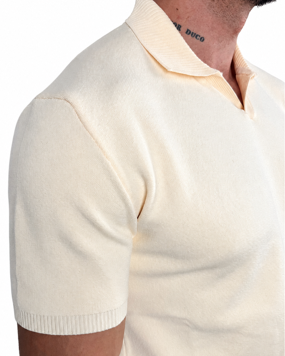 Close-up of a man wearing a cream-colored short-sleeve knit polo shirt, showing the ribbed collar and sleeve hem against a plain white background.