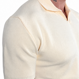 Close-up of a man wearing a cream-colored short-sleeve knit polo shirt, showing the ribbed collar and sleeve hem against a plain white background.