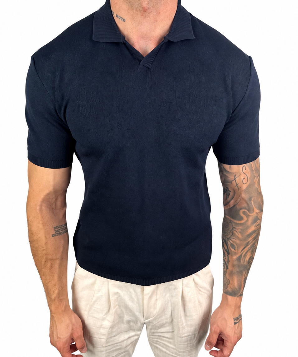 A man wearing a dark navy blue short-sleeve polo shirt and off-white trousers, shown from the neck down against a plain white background.
