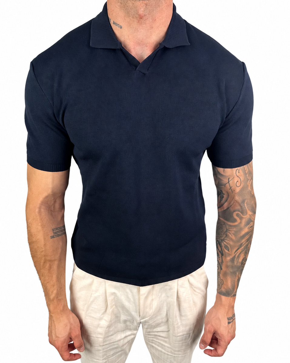A man wearing a dark navy blue short-sleeve polo shirt and off-white trousers, shown from the neck down against a plain white background.