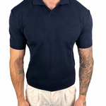 A man wearing a dark navy blue short-sleeve polo shirt and off-white trousers, shown from the neck down against a plain white background.