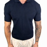A man wearing a dark navy blue short-sleeve polo shirt and off-white trousers, shown from the neck down against a plain white background.
