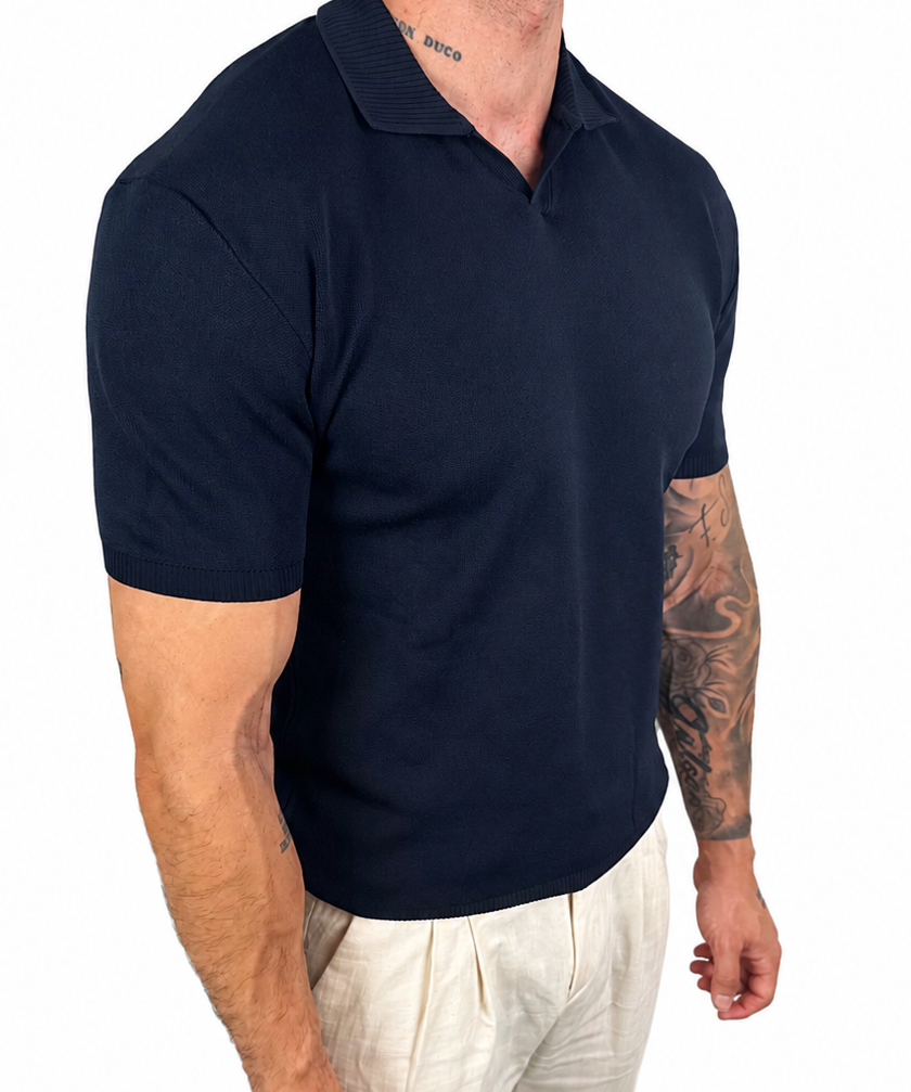 A muscular man wearing a dark navy blue short-sleeve polo shirt and off-white linen trousers, shown from the waist down against a solid white background.