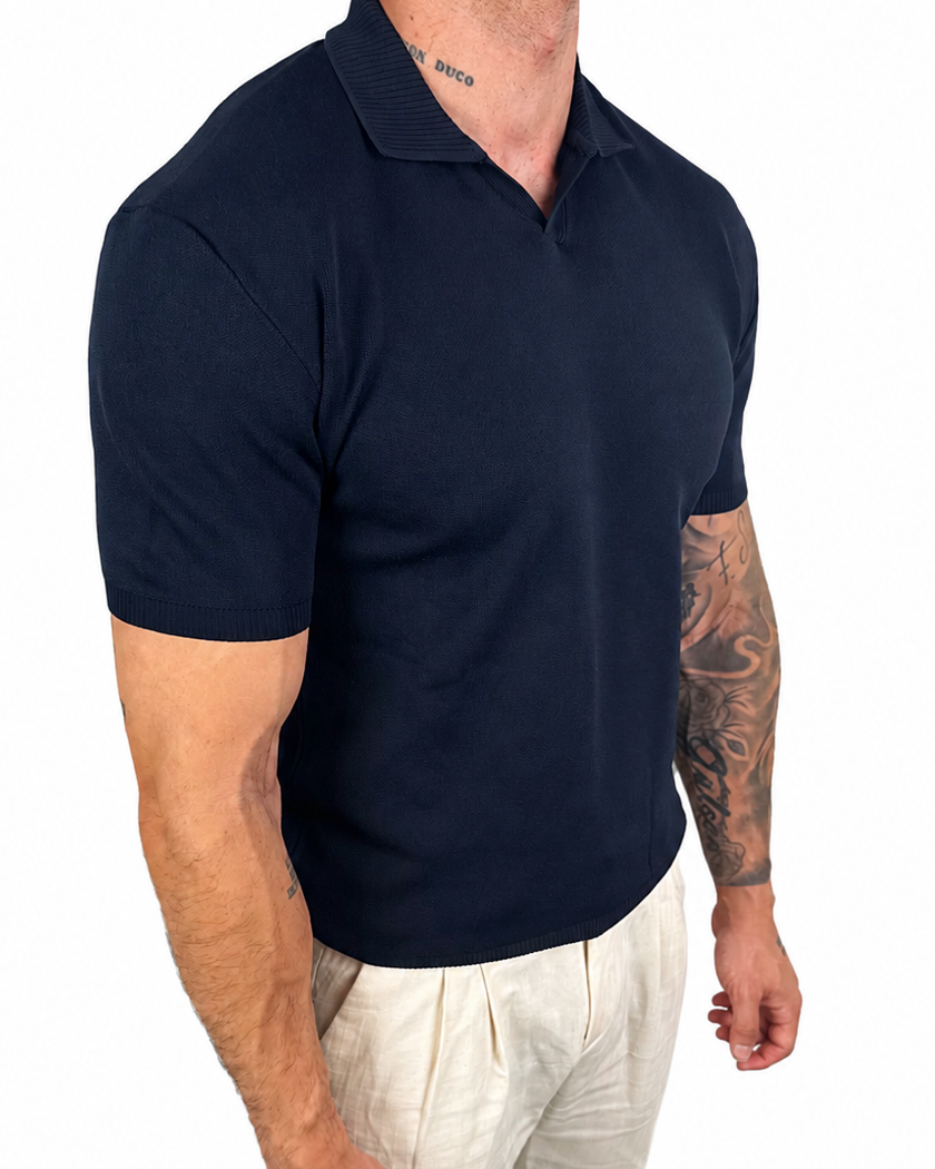 A muscular man wearing a dark navy blue short-sleeve polo shirt and off-white linen trousers, shown from the waist down against a solid white background.
