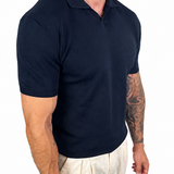 A muscular man wearing a dark navy blue short-sleeve polo shirt and off-white linen trousers, shown from the waist down against a solid white background.