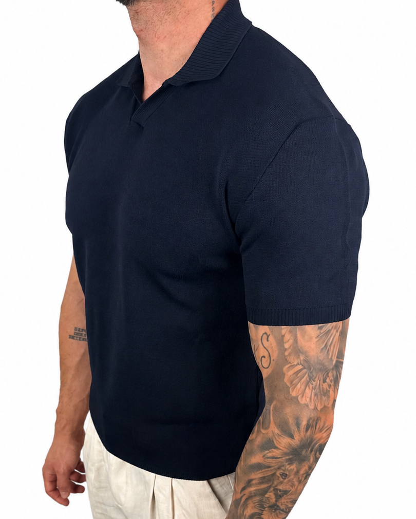 A man wearing a dark navy blue short-sleeve polo shirt and off-white trousers, shown from a side profile against a plain white background.