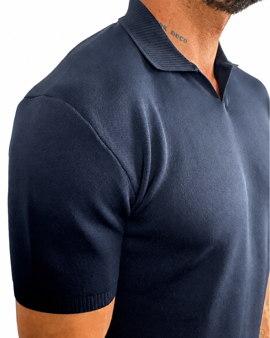 A close-up side view of a man wearing a dark navy blue short-sleeve knit polo shirt against a plain white background.