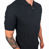 A man wearing a black short-sleeve polo shirt with vertical textured stripes and matching black pants, shown from the neck down against a plain white background.