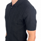 A man wearing a black short-sleeve polo shirt with vertical textured stripes and black pants, shown from the side against a plain white background.