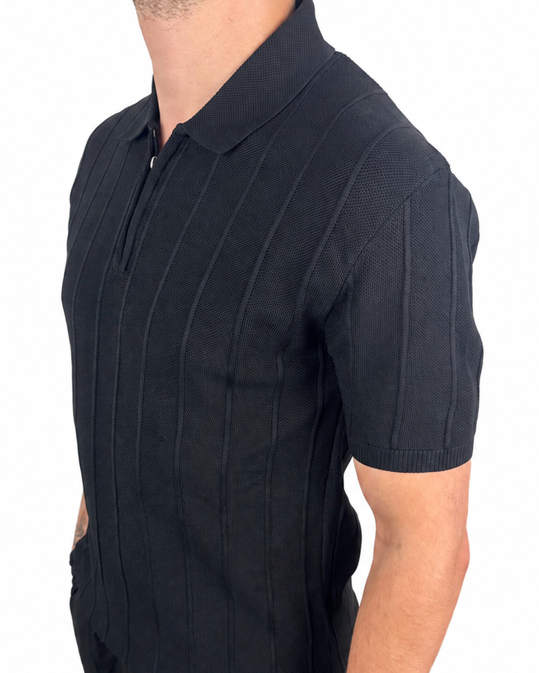 A man wearing a black short-sleeve polo shirt with vertical textured stripes and black pants, shown from the side against a plain white background.