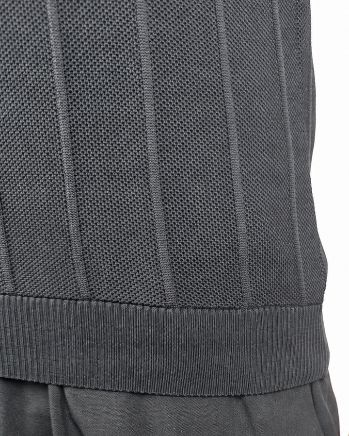 Close-up of a person wearing a dark gray ribbed knit top and dark gray pants, with the hand resting near the pocket, against a plain white background.