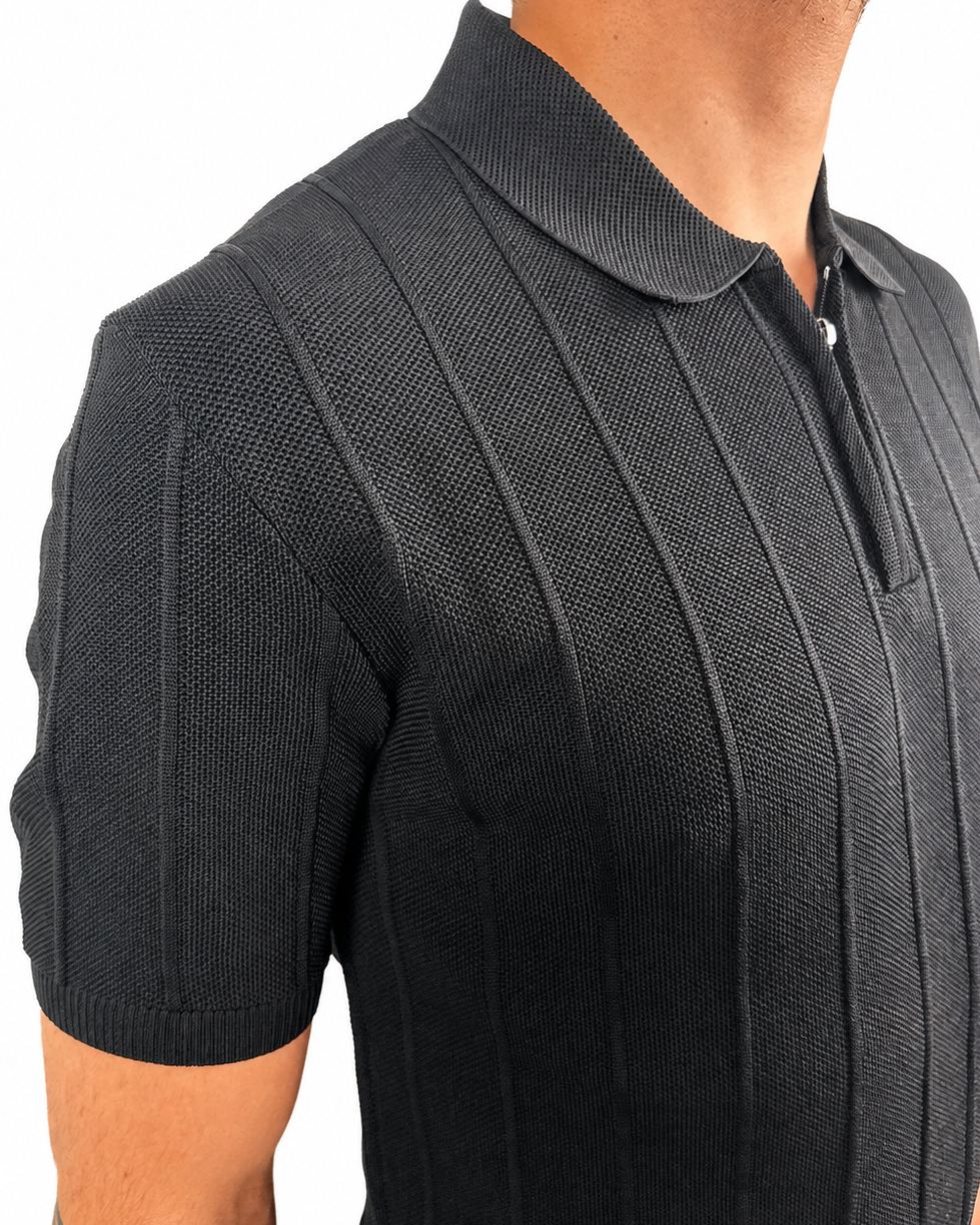 Close-up of a man wearing a black short-sleeve polo shirt with a textured knit pattern and a half-zip collar, shown against a plain white background.