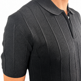 Close-up of a man wearing a black short-sleeve polo shirt with a textured knit pattern and a half-zip collar, shown against a plain white background.