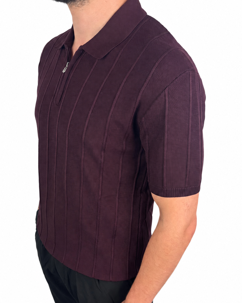 A man wearing a short-sleeve polo shirt in a deep plum purple color with vertical textured stripes, paired with black pants, shown from a side profile against a white background.