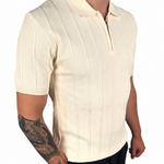 A man wearing a cream-colored short-sleeve knit polo shirt with vertical ribbed stripes and a half-zip collar, paired with black pants, shown against a plain white background.
