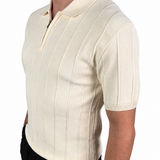 A man wearing a cream-colored short-sleeve knit polo shirt with vertical ribbed stripes and a half-zip collar, paired with black trousers, shown from a side profile against a white background.