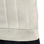 Close-up of a person wearing a cream ribbed knit sweater vest and black pants against a white background.