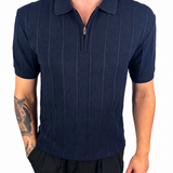 A man wearing a navy blue short-sleeve polo shirt with a vertical textured stripe pattern and a half-zip collar, paired with black pants, shown against a plain white background.