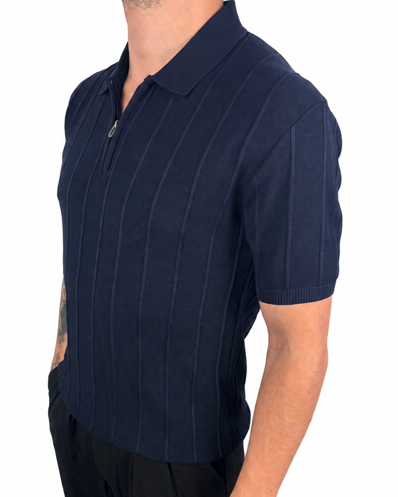 A man wearing a navy blue short-sleeve polo shirt with thin vertical pinstripes and a half-zip collar, paired with black pants, shown against a plain white background.