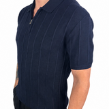 A man wearing a navy blue short-sleeve polo shirt with thin vertical pinstripes and a half-zip collar, paired with black pants, shown against a plain white background.