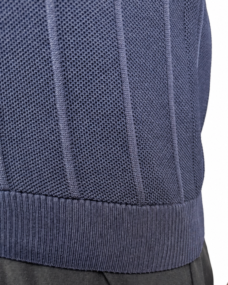 Close-up of a person wearing a navy ribbed knit top and dark pants, with the hand and arm visible against a plain white background.