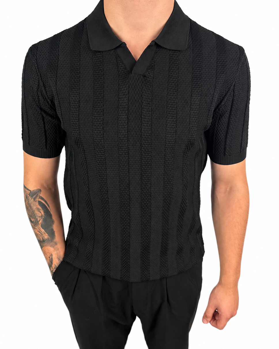 A man wearing a black short-sleeve polo shirt with a textured vertical stripe pattern and black pants, shown from the neck down against a plain white background.