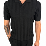 A man wearing a black short-sleeve polo shirt with a textured vertical stripe pattern and black pants, shown from the neck down against a plain white background.