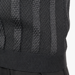 Close-up of a person wearing a dark charcoal gray knit sweater vest with vertical textured stripes and black trousers, against a plain white background.