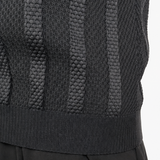 Close-up of a person wearing a dark charcoal gray knit sweater vest with vertical textured stripes and black trousers, against a plain white background.