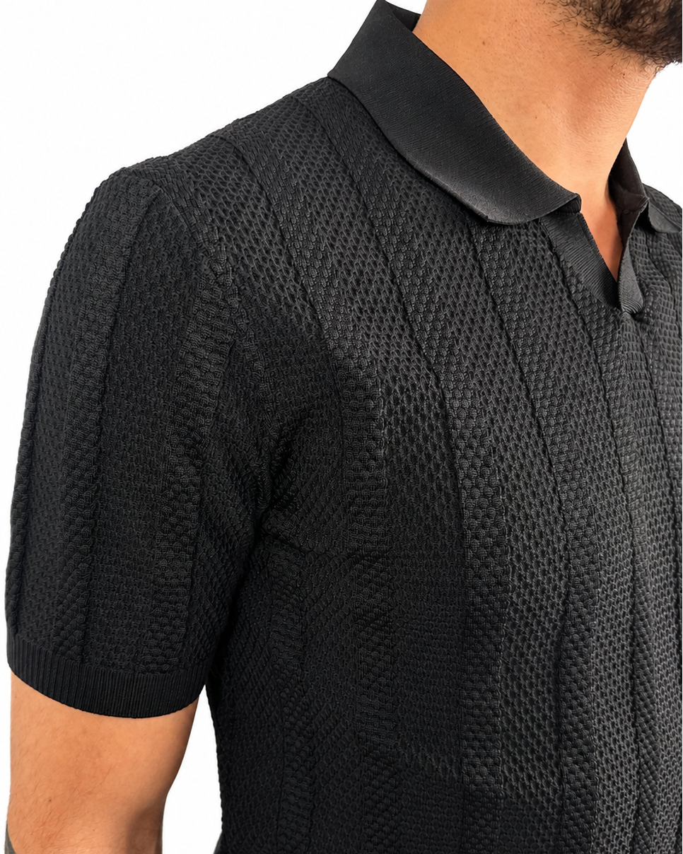 Close-up of a man wearing a black short-sleeve textured knit polo shirt with a contrasting black collar, shown against a plain white background.