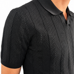 Close-up of a man wearing a black short-sleeve textured knit polo shirt with a contrasting black collar, shown against a plain white background.
