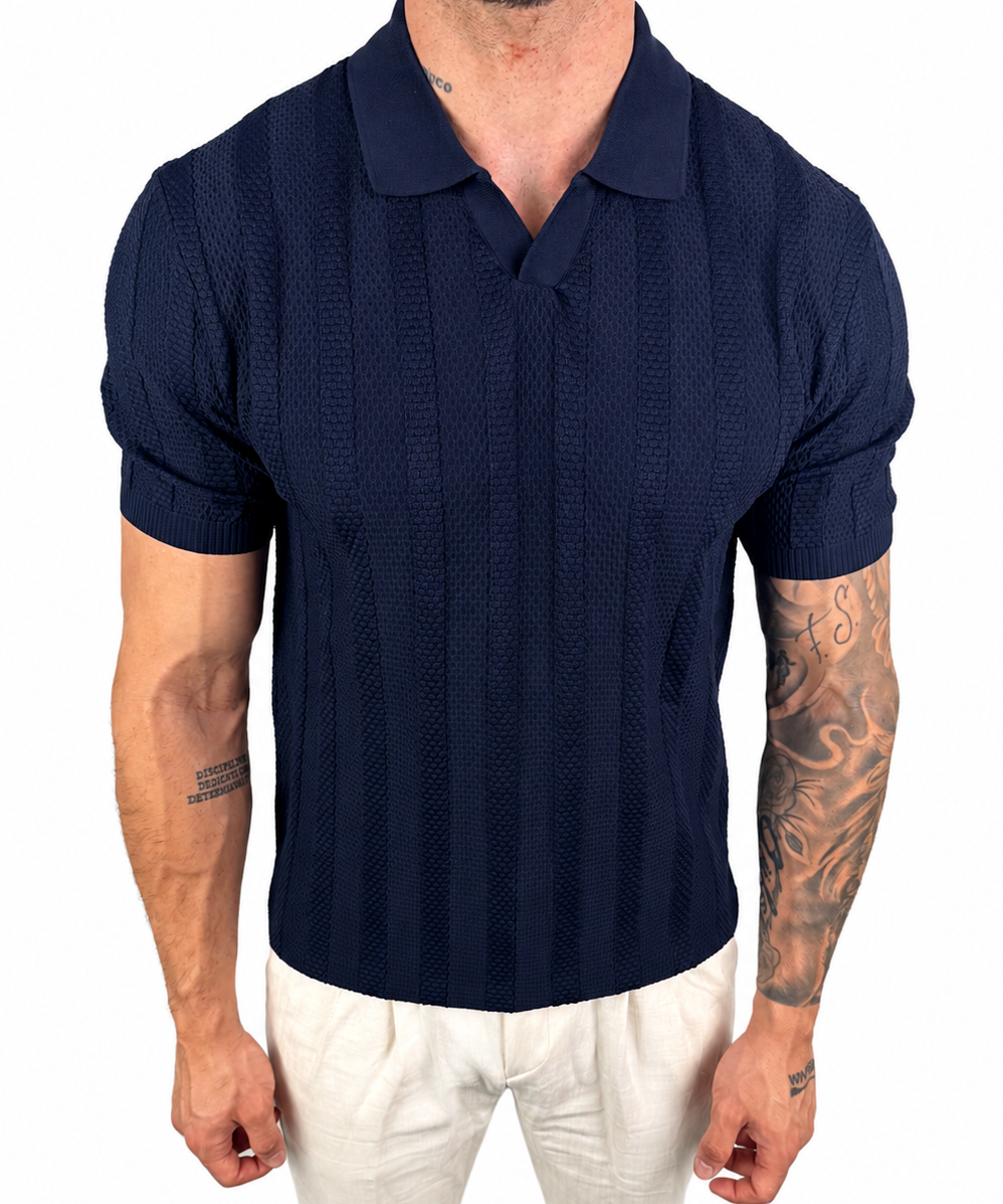 A man wearing a navy blue short-sleeve polo shirt with a textured knit pattern and white pants, shown from the neck down against a plain white background.