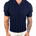 A man wearing a navy blue short-sleeve polo shirt with a textured knit pattern and white pants, shown from the neck down against a plain white background.