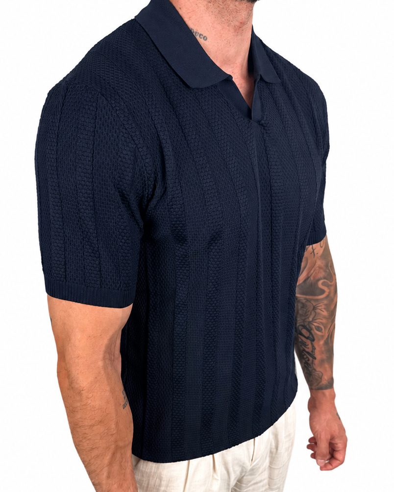 A man wearing a dark navy blue short-sleeve polo shirt with a textured knit pattern and light beige trousers, shown from a side profile against a white background.