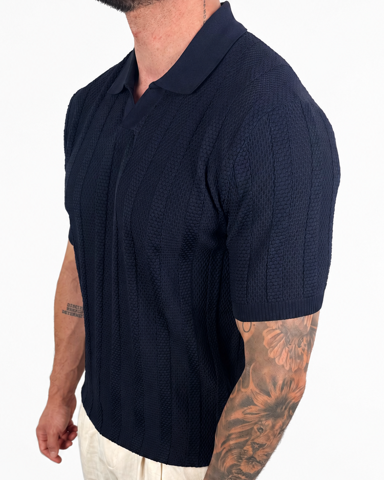 A man wearing a dark navy blue short-sleeve knit polo shirt and light beige pants, shown from the waist up against a plain white background.