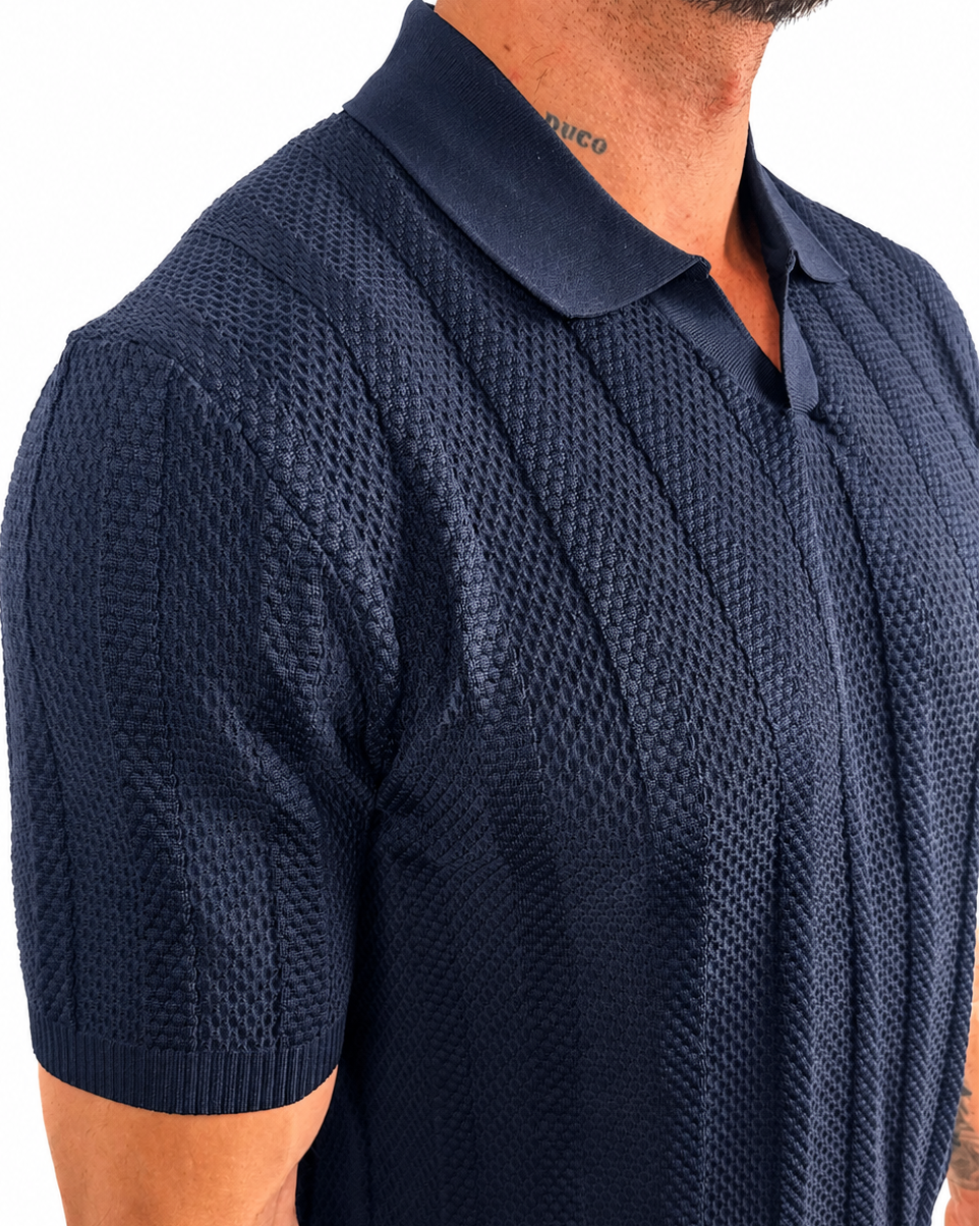 A close-up of a man wearing a navy blue short-sleeve polo shirt with a textured waffle knit pattern, shown from the chest down against a plain white background.