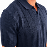 A close-up of a man wearing a navy blue short-sleeve polo shirt with a textured waffle knit pattern, shown from the chest down against a plain white background.