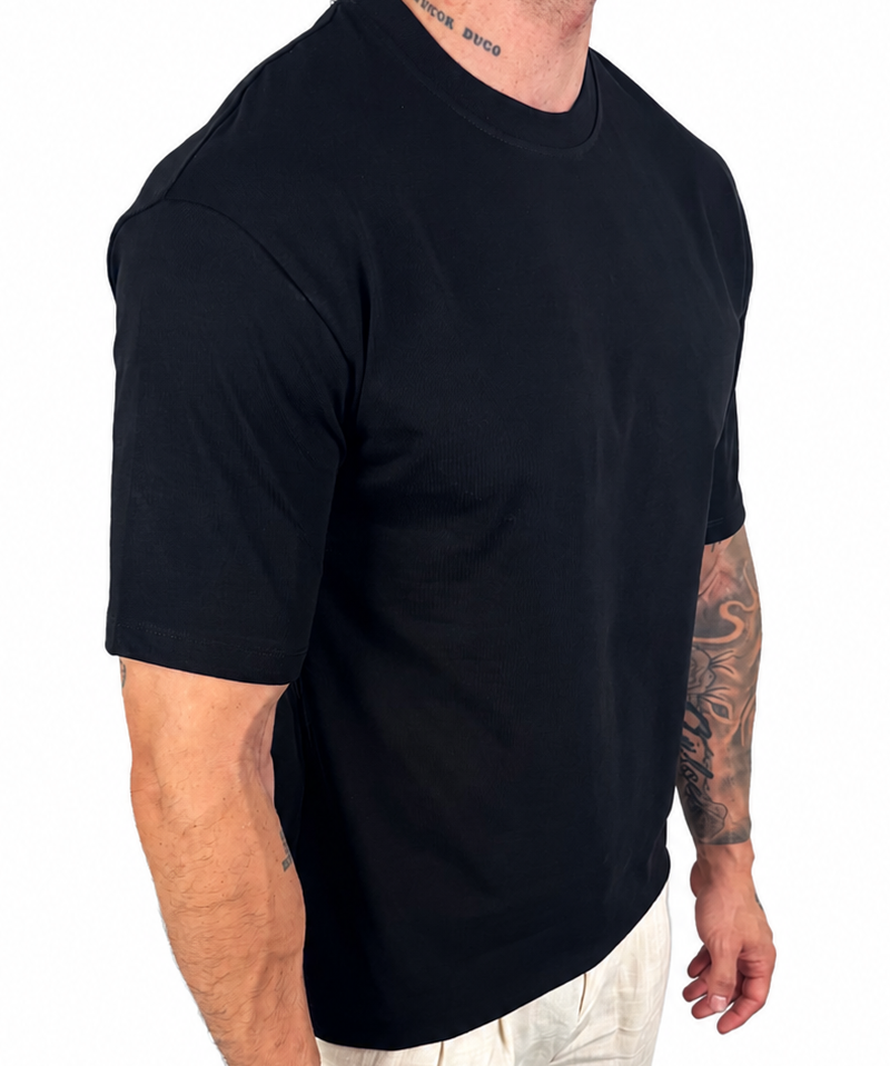 A man wearing a black short-sleeve crewneck t-shirt and off-white linen pants, shown from a side-back angle against a plain white background.