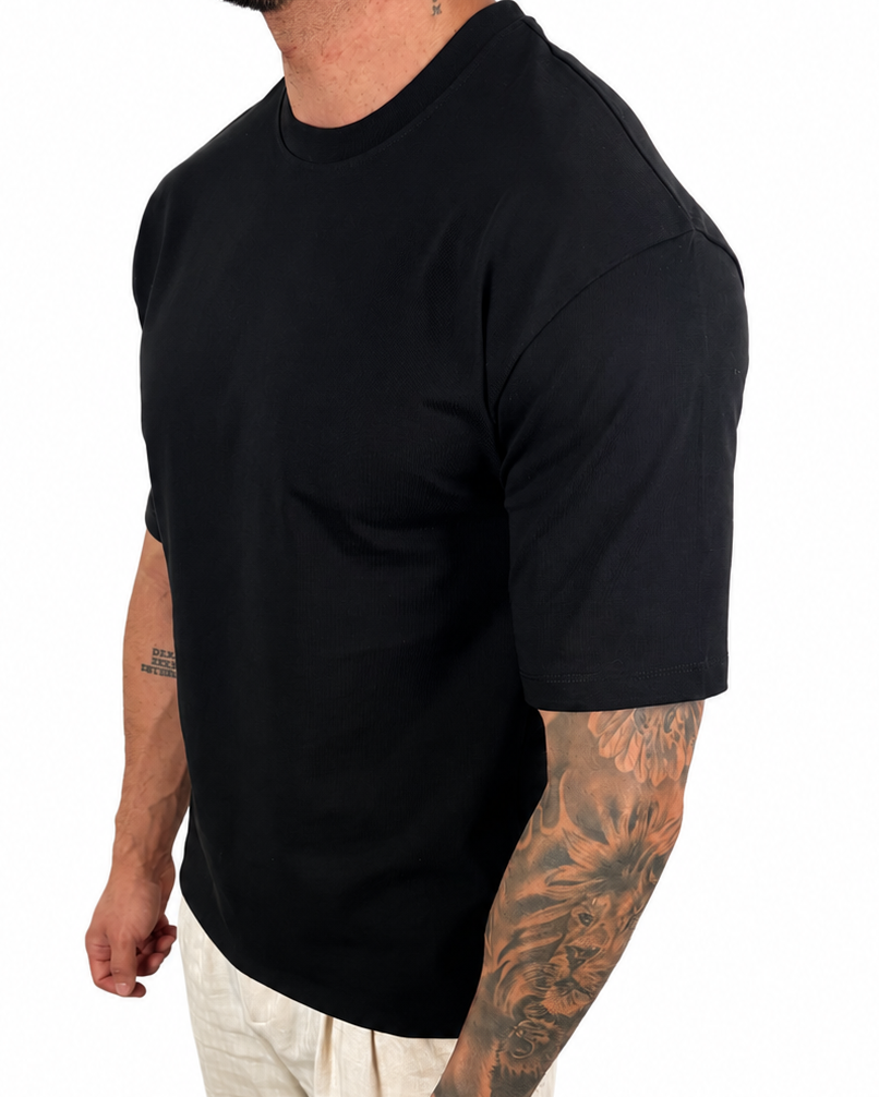 A man wearing a plain black short-sleeve crewneck t-shirt and light beige pants, shown from a side/back angle against a solid white background.