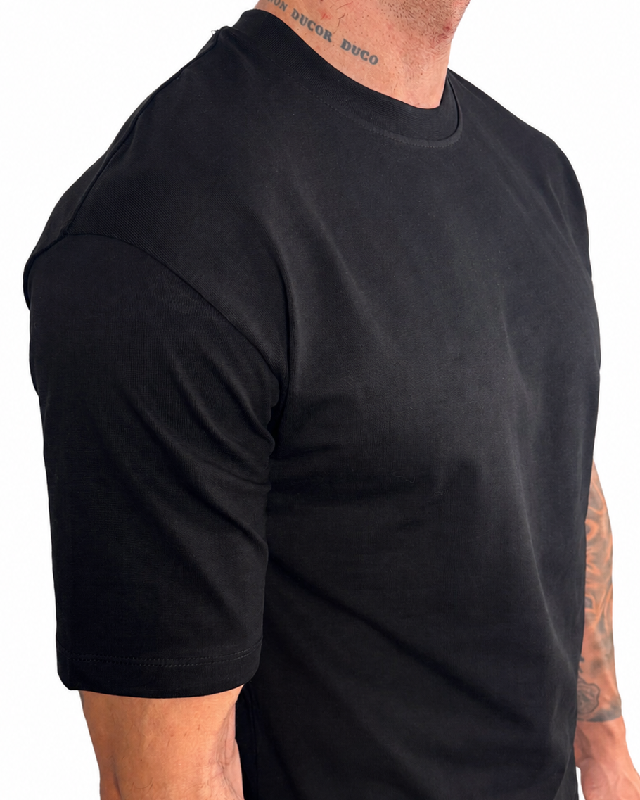A man wearing a plain black short-sleeve crewneck t-shirt, shown from a side profile against a white background.