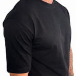 A man wearing a plain black short-sleeve crewneck t-shirt, shown from a side profile against a white background.